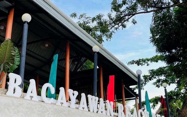 The shore pavilion at Bacayawan Beach Resort, Barangay Bacayawan, Dimataling, with the resort name spelled out in white letters along the sea wall.