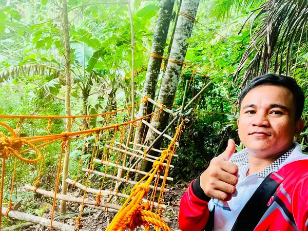 A man giving a thumbs up beside a completed rope and timber pioneering bridge in the forest